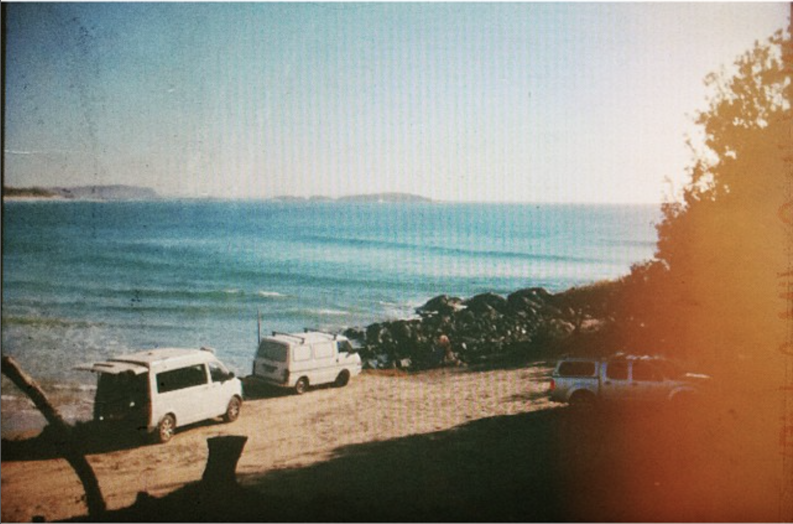Grainy archival photo of vans parked beside a quiet Australian beach in the morning.